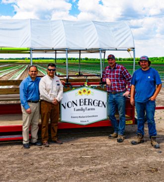 a group of men standing beside a farm trailer